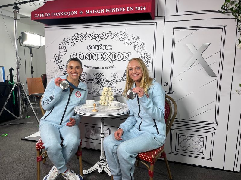 Two Team USA athletes displaying their medals at the Xfinity Connections Cafe.
